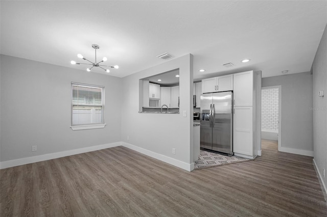 kitchen with kitchen peninsula, stainless steel refrigerator with ice dispenser, hardwood / wood-style flooring, a notable chandelier, and white cabinets