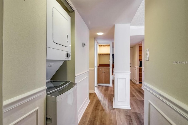 clothes washing area with stacked washing maching and dryer, light hardwood / wood-style floors, and decorative columns