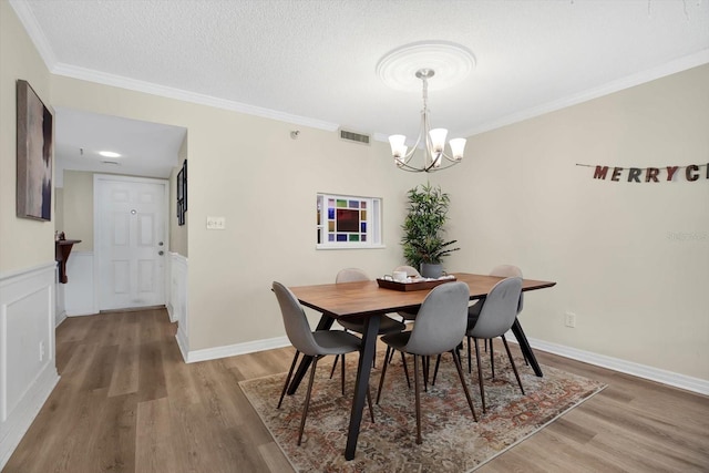 dining area with an inviting chandelier, ornamental molding, a textured ceiling, and light wood-type flooring