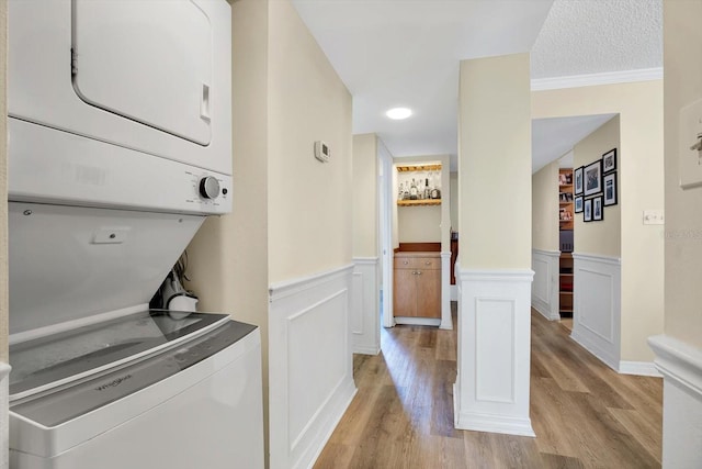 laundry area featuring stacked washing maching and dryer, decorative columns, light wood-type flooring, crown molding, and a textured ceiling