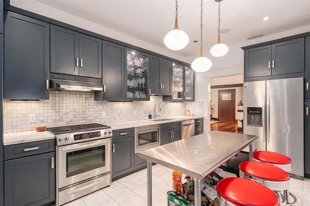 kitchen featuring sink, light stone counters, backsplash, decorative light fixtures, and appliances with stainless steel finishes