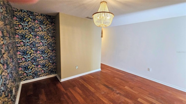 empty room with dark wood-type flooring and an inviting chandelier