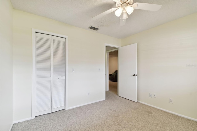 unfurnished bedroom featuring a textured ceiling, a closet, ceiling fan, and light colored carpet