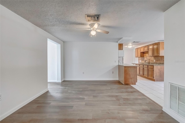 unfurnished living room featuring a textured ceiling, light hardwood / wood-style flooring, ceiling fan, and sink