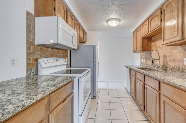 kitchen featuring white appliances, backsplash, light stone counters, and sink