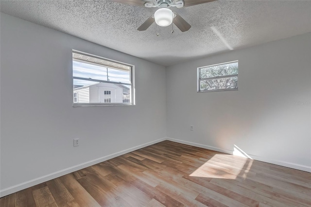 empty room with ceiling fan, wood-type flooring, a textured ceiling, and a wealth of natural light