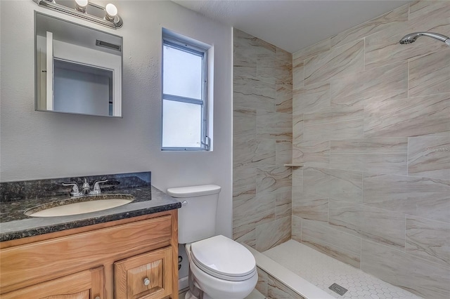 bathroom with tiled shower, vanity, and toilet