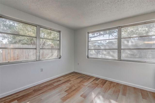 empty room featuring a textured ceiling, light hardwood / wood-style flooring, and a healthy amount of sunlight