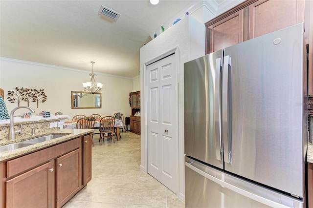 kitchen featuring light stone countertops, ornamental molding, sink, a chandelier, and stainless steel refrigerator