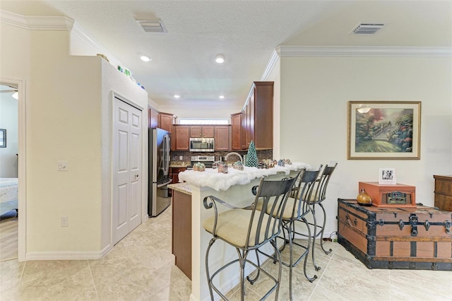 kitchen featuring kitchen peninsula, a kitchen bar, backsplash, stainless steel appliances, and crown molding