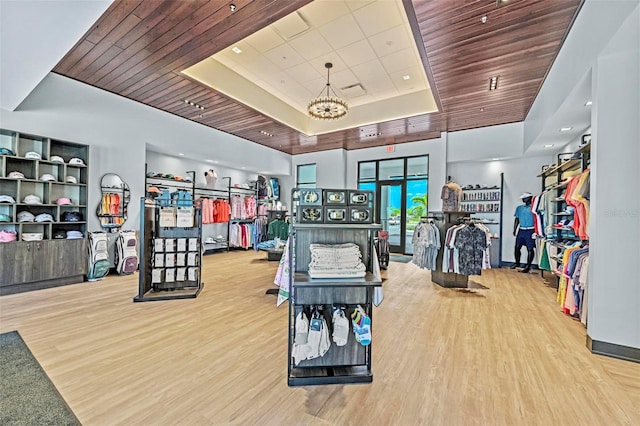 gym featuring hardwood / wood-style flooring, a notable chandelier, wood ceiling, and a tray ceiling