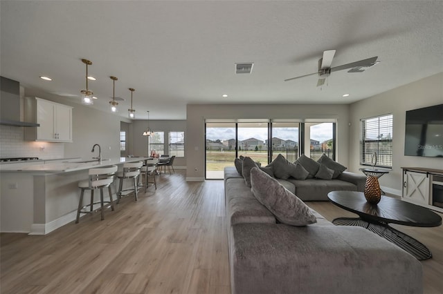 living room with visible vents, light wood-style floors, a ceiling fan, a textured ceiling, and baseboards