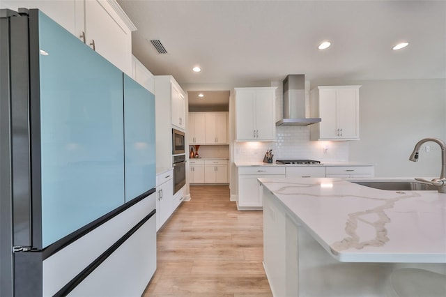 kitchen featuring visible vents, light wood-style floors, a sink, wall chimney range hood, and built in appliances