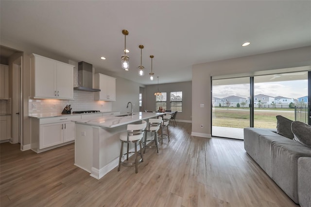 kitchen with decorative backsplash, wall chimney exhaust hood, a breakfast bar, open floor plan, and black cooktop