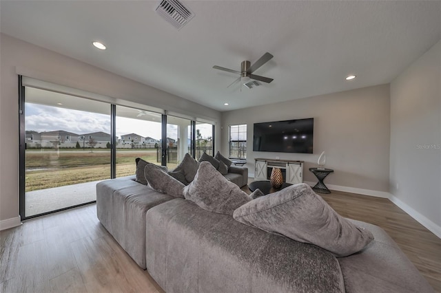 living room with baseboards, visible vents, ceiling fan, and light wood finished floors