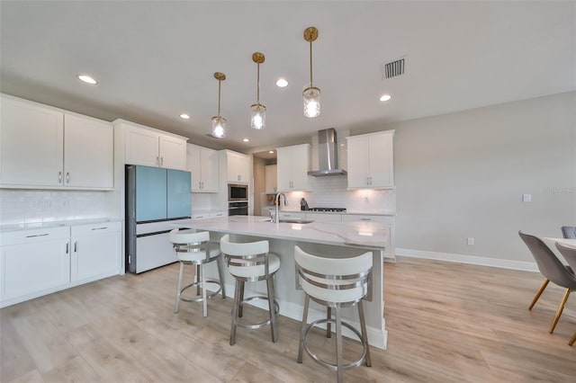 kitchen featuring freestanding refrigerator, white cabinets, a sink, and wall chimney range hood