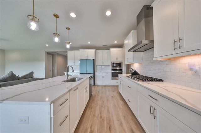 kitchen featuring white cabinets, light wood-style floors, stainless steel appliances, wall chimney range hood, and a sink