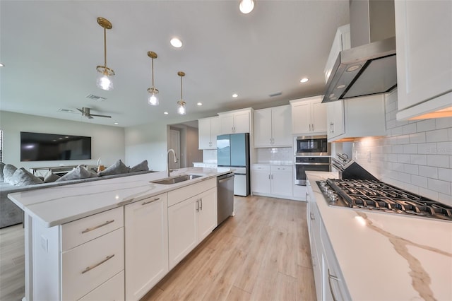 kitchen with wall chimney exhaust hood, open floor plan, stainless steel appliances, white cabinetry, and a sink