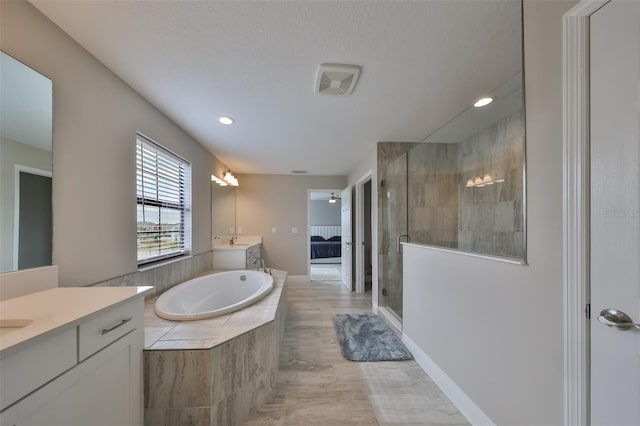 full bath with two vanities, a shower stall, a textured ceiling, and a bath