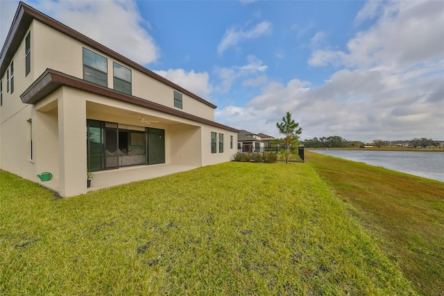 back of property featuring a lawn, a water view, and stucco siding