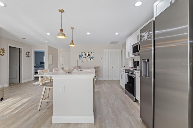 kitchen featuring a breakfast bar area, stainless steel appliances, an island with sink, hanging light fixtures, and white cabinetry