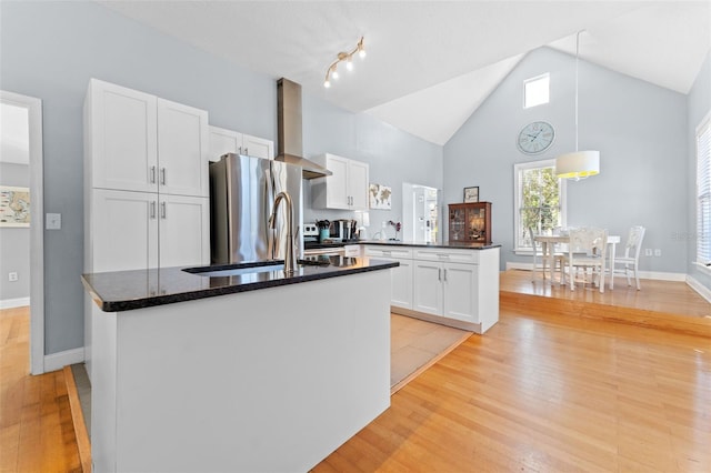 kitchen with wall chimney range hood, light wood-type flooring, a kitchen island, white cabinetry, and stainless steel refrigerator