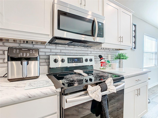 kitchen featuring backsplash, light hardwood / wood-style flooring, light stone countertops, white cabinetry, and stainless steel appliances