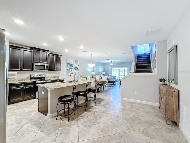 kitchen with ceiling fan, decorative light fixtures, a breakfast bar, a center island with sink, and appliances with stainless steel finishes