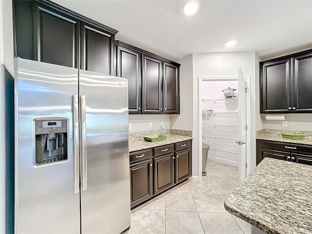 kitchen with stainless steel fridge, light stone countertops, light tile patterned floors, and a textured ceiling