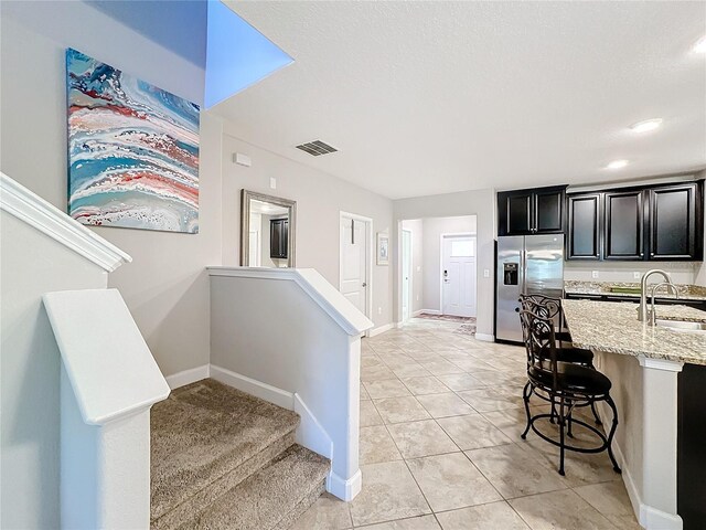 kitchen featuring light stone countertops, a kitchen breakfast bar, sink, light tile patterned floors, and stainless steel fridge with ice dispenser