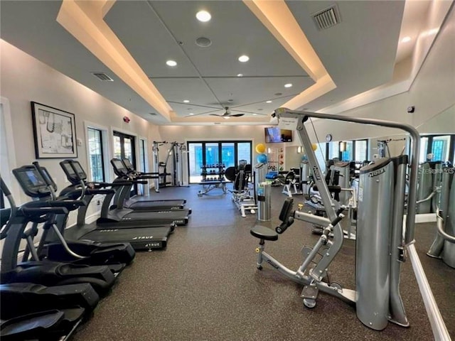 gym with a tray ceiling and ceiling fan