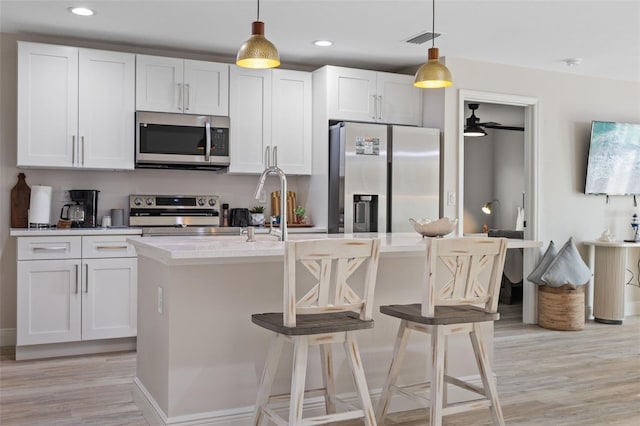 kitchen with stainless steel appliances, decorative light fixtures, white cabinets, a kitchen island with sink, and a breakfast bar