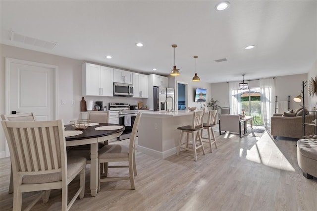 kitchen featuring white cabinetry, a kitchen island with sink, stainless steel appliances, pendant lighting, and light hardwood / wood-style flooring