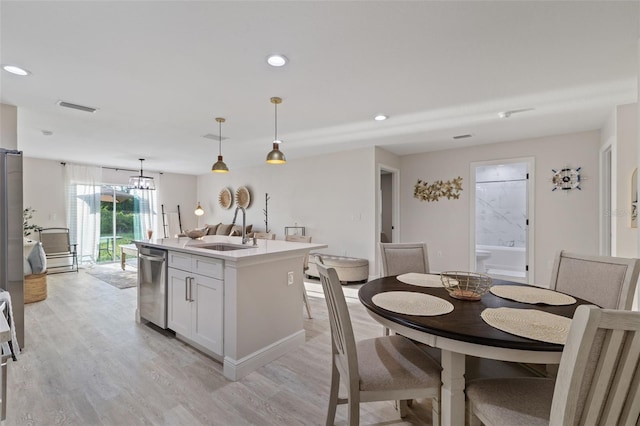 kitchen with light hardwood / wood-style floors, an island with sink, pendant lighting, sink, and stainless steel dishwasher