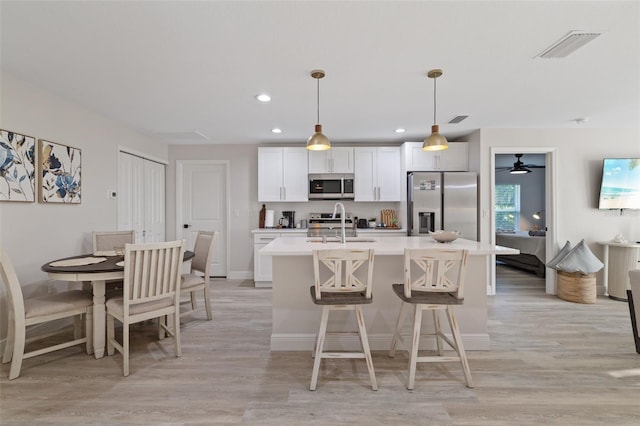 kitchen with stainless steel appliances, decorative light fixtures, light wood-type flooring, and a kitchen island with sink