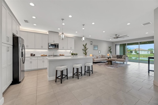 kitchen with a breakfast bar, white cabinetry, an island with sink, pendant lighting, and stainless steel appliances