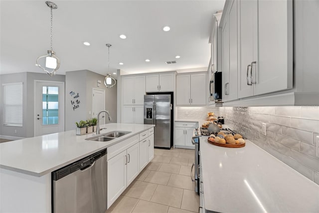 kitchen featuring decorative light fixtures, a sink, light countertops, appliances with stainless steel finishes, and a center island with sink