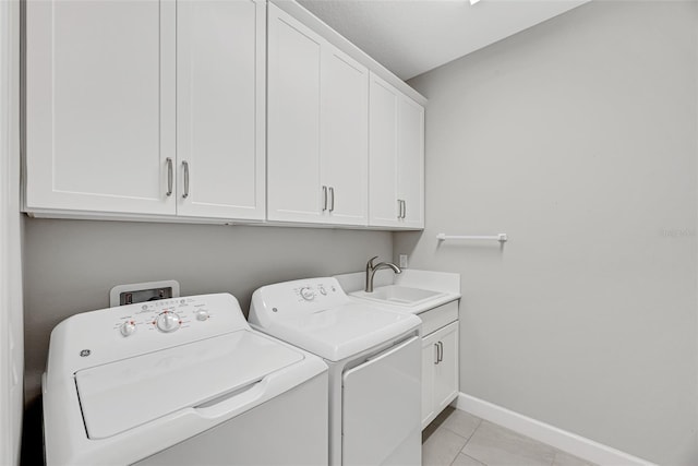 laundry room featuring light tile patterned floors, cabinet space, washing machine and dryer, a sink, and baseboards