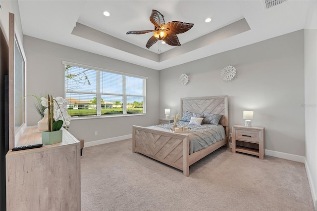 bedroom with baseboards, visible vents, a tray ceiling, and light colored carpet