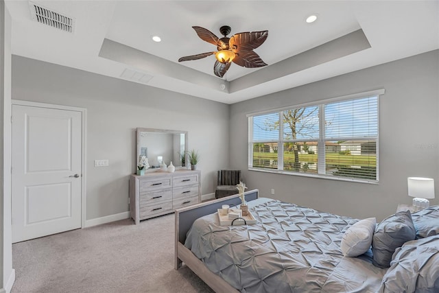 bedroom with ceiling fan, light carpet, visible vents, baseboards, and a tray ceiling