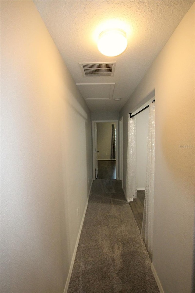 hallway with dark carpet and a textured ceiling