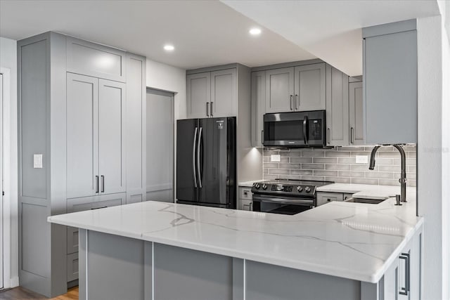 kitchen featuring gray cabinetry, light stone countertops, kitchen peninsula, decorative backsplash, and appliances with stainless steel finishes