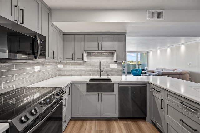 kitchen with light stone countertops, gray cabinetry, stainless steel appliances, sink, and light hardwood / wood-style flooring