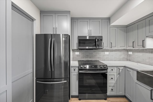 kitchen with backsplash, gray cabinets, light stone countertops, and stainless steel appliances