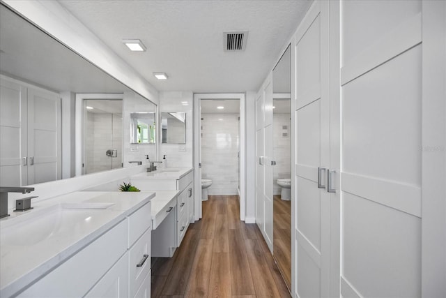 bathroom with hardwood / wood-style floors, vanity, toilet, a textured ceiling, and a shower with shower door