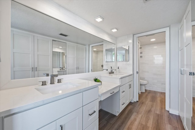 bathroom with vanity, hardwood / wood-style flooring, toilet, tile walls, and a textured ceiling