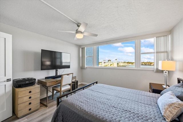 bedroom with a textured ceiling, light wood-type flooring, multiple windows, and ceiling fan