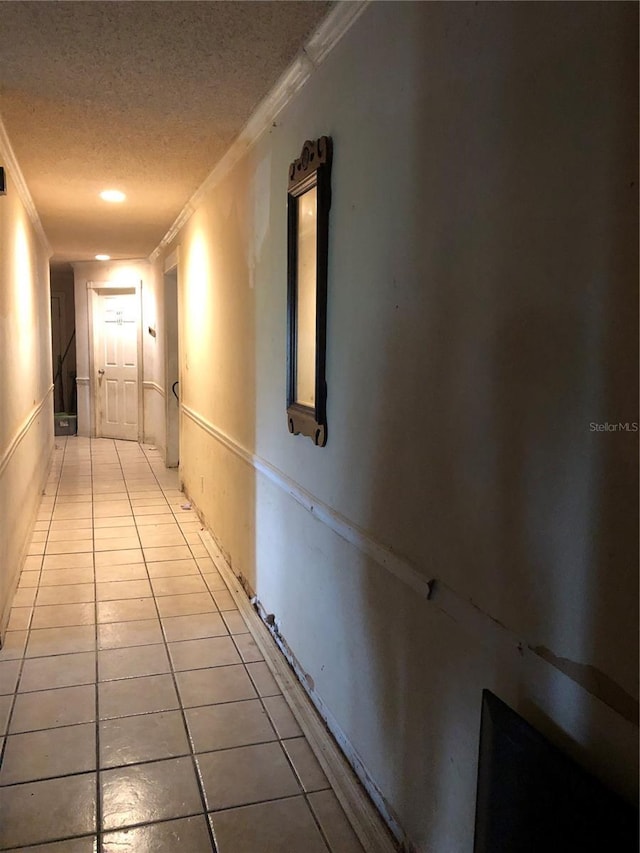 corridor featuring light tile patterned floors, a textured ceiling, and ornamental molding