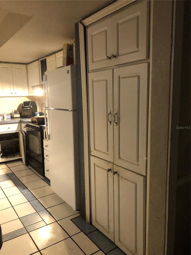 kitchen featuring white refrigerator, light tile patterned flooring, white cabinetry, and black electric range