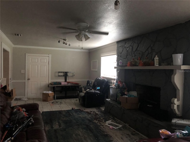 living room featuring ceiling fan, a stone fireplace, crown molding, a textured ceiling, and light tile patterned floors